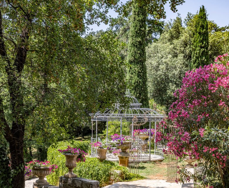 Ein malerischer Gartenweg führt zu einem eleganten Pavillon, umgeben von üppigem Grün und bunten Blumen. Die Atmosphäre ist ruhig und einladend, ideal für entspannende Spaziergänge in der Natur.