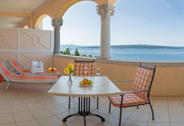 Ein Balkon mit Blick auf das Meer, ausgestattet mit einem Tisch und zwei Stühlen sowie einer Liege. Auf dem Tisch stehen frisches Obst und eine Blumenvase. Die Atmosphäre ist entspannt und einladen... Doppelzimmer im Hotel direkt am Meer, Crikvenica