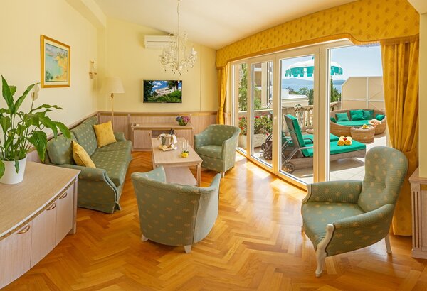 Heller Wohnbereich mit bequemen Möbeln in sanften Farben. Eine große Fensterfront führt zu einem Balkon mit Liegen und Blick auf die Landschaft. Pflanzen und dekorative Elemente schaffen eine einla... Hotel mit Appartements für Familien, Kroatien - am Meer