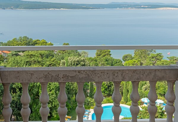 Blick von einem Balkon auf eine ruhige Küstenlandschaft mit grünem Uferbewuchs und einem blauen Pool im Vordergrund. Im Hintergrund erstreckt sich das Wasser bis zum Horizont, umgeben von sanften H... Doppelzimmer mit Meerblick im Strandhotel Crikvenica