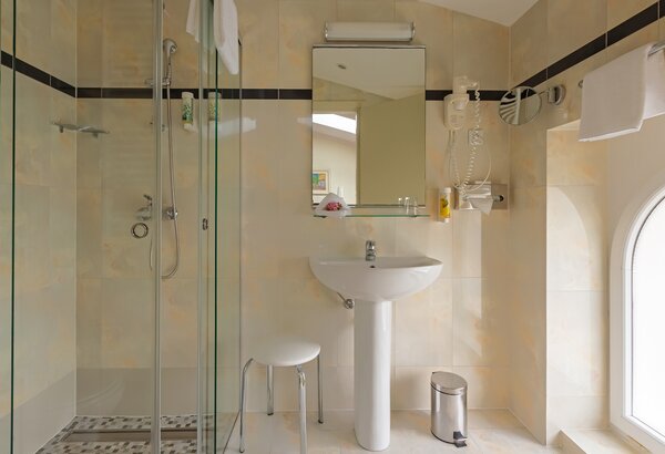 Moderne Badezimmeransicht mit einer gläsernen Dusche, einem Waschbecken und einem Spiegel. Helle Fliesen und ein Fenster sorgen für eine freundliche Atmosphäre. Ein Hocker und ein Mülleimer ergänze... Einzelzimmer im historischen Hotel in Crikvenica