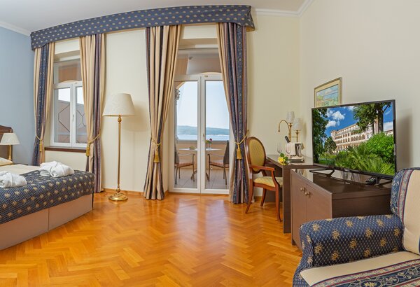 Ein helles Hotelzimmer mit einem Doppelbett, einem Fernseher und einem gemütlichen Sessel. Große Fenster mit Blick auf einen Balkon und die Landschaft. Der Boden ist aus Holz, und die Wände sind in... Doppelzimmer im Hotel direkt am Meer, Crikvenica
