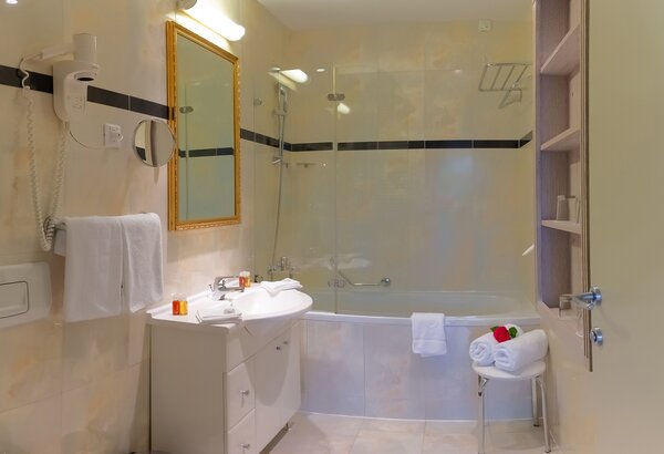 Modernes Badezimmer mit Badewanne, Waschbecken und Spiegel. Helle Fliesen und eine große Dusche sorgen für eine einladende Atmosphäre. Handtücher und Pflegeprodukte sind ordentlich platziert. Ein d... Wunderschöne Zimmer im Familienhotel Crikvenica