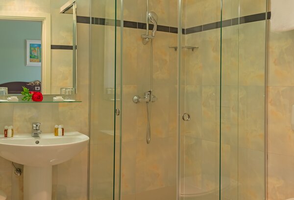 Modernes Badezimmer mit gläserner Duschkabine, Waschbecken und Spiegel. Sanfte Farben an den Wänden und eine kleine Blumendekoration auf dem Waschbecken schaffen eine einladende Atmosphäre. Romantikurlaub Kroatien in den schönen Doppelzimmern