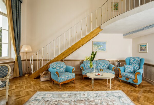 Gemütlicher Wohnbereich mit blauen Polstersesseln und einem kleinen Tisch. Eine Treppe führt in den oberen Bereich, während große Fenster viel Tageslicht hereinlassen. Der Boden ist aus Holz, und e... Kaiserliche Suiten im Hotel mit Meerblick Kroatien
