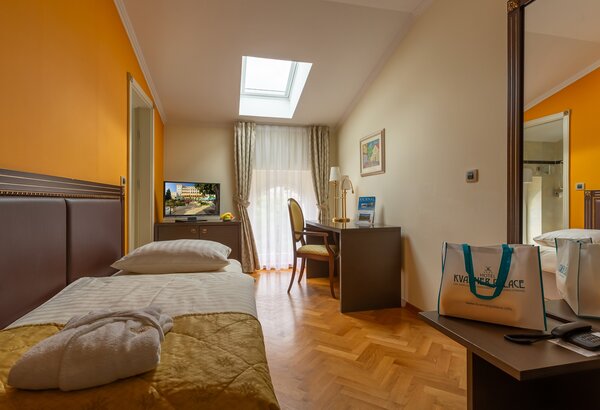 Ein gemütliches Hotelzimmer mit einem Einzelbett, einem Schreibtisch und einem Stuhl. Ein Fernseher steht auf einem Sideboard, und große Fenster lassen Tageslicht herein. Die Wände sind in warmen O... Einzelzimmer im historischen Hotel in Crikvenica
