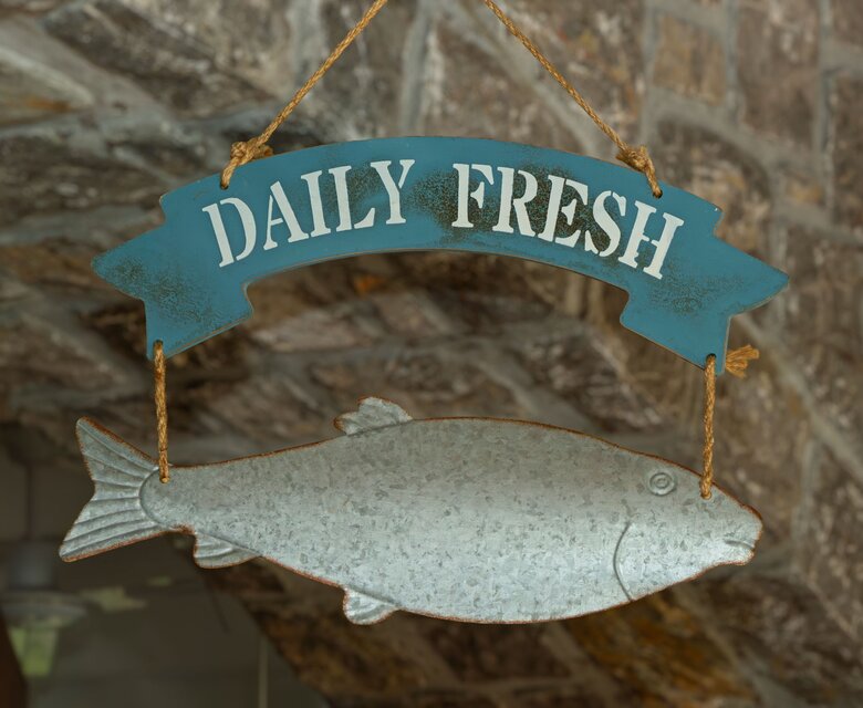 Ein hängendes Schild mit der Aufschrift "DAILY FRESH" über einem stilisierten Fisch. Der Hintergrund zeigt eine steinerne Wand, die eine rustikale Atmosphäre vermittelt.