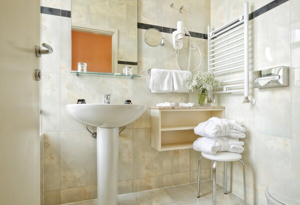 Helles Badezimmer mit modernen Fliesen, einem Waschbecken, Handtüchern und einem Handtuchhalter. Eine kleine Ablage mit frischen Blumen und Toilettenartikeln ergänzt die Einrichtung. Historisches Hotel, Kroatien - Ihr Komfort-Einzelzimmer