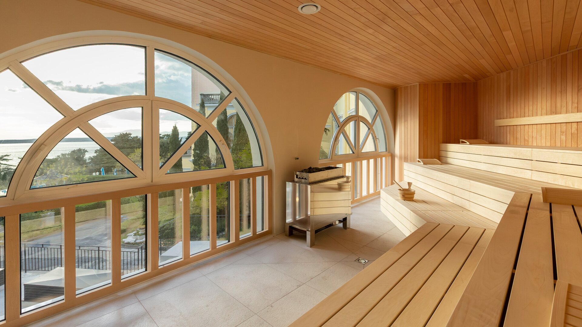 Helle Sauna mit großen Fenstern, die einen Blick auf die Landschaft bieten. Die Wände und Bänke sind aus hellem Holz, und der Raum strahlt eine entspannende Atmosphäre aus.
