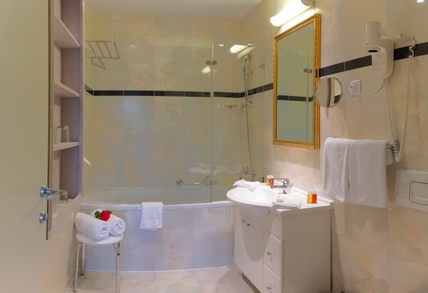 Helles Badezimmer mit Badewanne und Dusche, einem Waschbecken mit Spiegel und Handtüchern. Ein Stuhl mit frischen Handtüchern und dekorativen Elementen sorgt für eine einladende Atmosphäre. Familienurlaub Kroatien ist so schön im Kvarner Palace