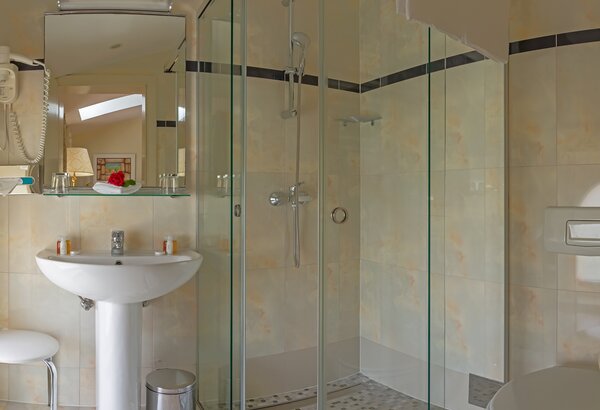 Moderne Dusche in einem hellen Badezimmer mit Glaswänden, einem Waschbecken auf einem weißen Standfuß, einem Spiegel und einem Hocker. Die Wände sind in sanften Farben gehalten, und der Boden ist g... Kvarner Bucht - Urlaub im Komfort Doppelzimmer