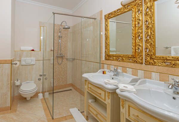 Elegantes Badezimmer mit zwei Waschbecken, goldverzierten Spiegeln und einer modernen Dusche in einer Glasabtrennung. Die Wände sind in sanften Beigetönen gehalten, und der Boden ist aus hellen Fli... Familienfreundliche Suite in Kroatien für Ihren Urlaub