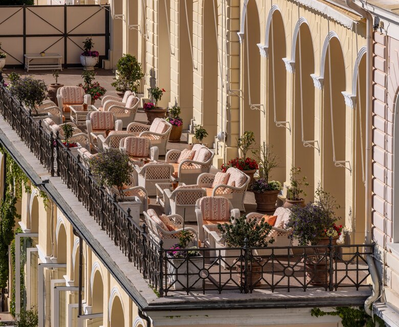 Eine elegante Terrasse mit bequemen Sitzgelegenheiten und blühenden Pflanzen, umgeben von einer hellen, historischen Fassade. Die Atmosphäre ist einladend und entspannend, ideal für Gäste, die die Aussicht genießen möchten.