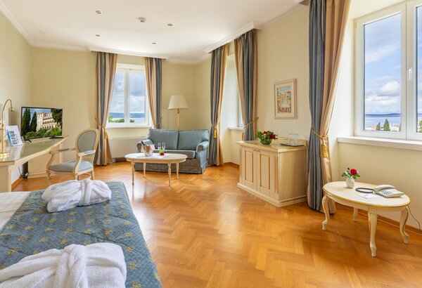 Helles Hotelzimmer mit Parkettboden, einem großen Fenster und Blick auf die Landschaft. Es gibt ein bequemes Sofa, einen Tisch mit Blumen, einen Fernseher und einen Schreibtisch. Die Wände sind in ... 4-Sterne-Hotel am Meer Kroatien ☛ Superior Doppelzimmer
