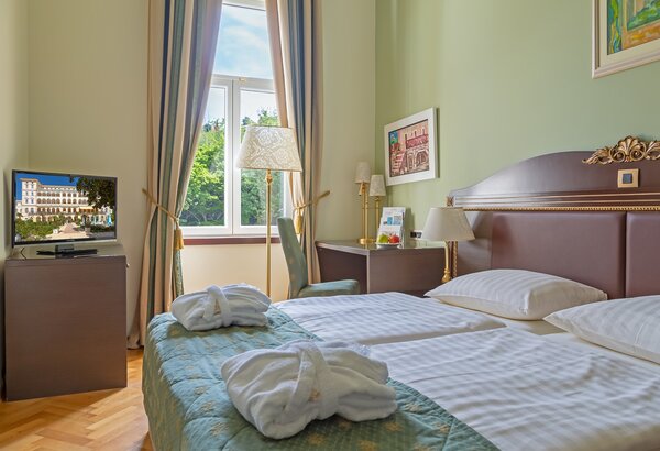 Ein helles Hotelzimmer mit zwei Einzelbetten, einem Fernseher und einem Fenster mit Blick ins Freie. Auf dem Bett liegen zwei weiße Bademäntel. Die Wände sind in sanften Farben gehalten, und es gib... Romantikurlaub Kroatien in den schönen Doppelzimmern