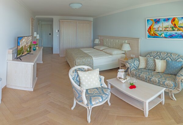 Helles Hotelzimmer mit einem großen Bett, einem gemütlichen Sofa und einem Couchtisch. Ein Fernseher steht auf einem Sideboard, und ein farbenfrohes Kunstwerk hängt an der Wand. Der Boden ist aus H... Doppelzimmer im Hotel direkt am Meer, Crikvenica