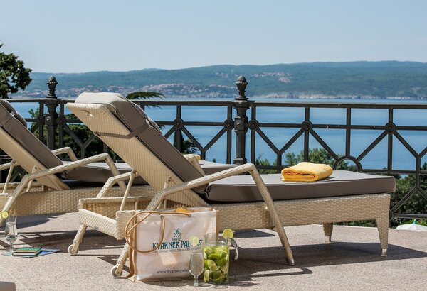Zwei Liegen stehen auf einer Terrasse mit Blick auf das Wasser und die umliegenden Hügel. Eine Liege hat ein gelbes Handtuch und eine Tüte mit frischen Früchten daneben. Die Atmosphäre ist entspann... Kaiserliche Suiten im Hotel mit Meerblick Kroatien