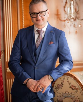 Domaćin u plavom odijelu stoji u elegantnom hotelskom interijeru pokraj tapecirane fotelje.