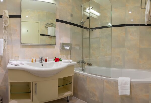 Modernes Badezimmer mit einer Badewanne und einer Dusche. Ein elegives Waschbecken mit Spiegel und Pflegeprodukten. Handtücher und ein kleiner Blumenstrauß auf der Ablage. Helle, freundliche Fliese... Hotel mit Meerblick in der Kvarner Bucht - Doppelzimmer