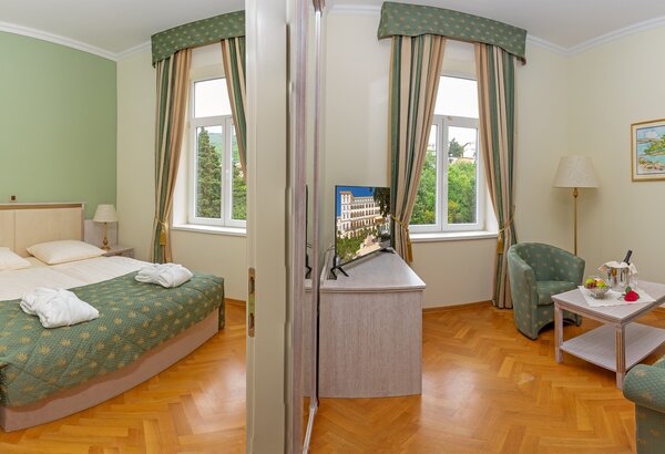 Helles Hotelzimmer mit einem Doppelbett, einem Tisch und zwei Stühlen. Große Fenster lassen viel Tageslicht herein, und die Wände sind in sanften Farben gehalten. Eine gemütliche Atmosphäre mit Bli... Wunderschöne Zimmer im Familienhotel Crikvenica