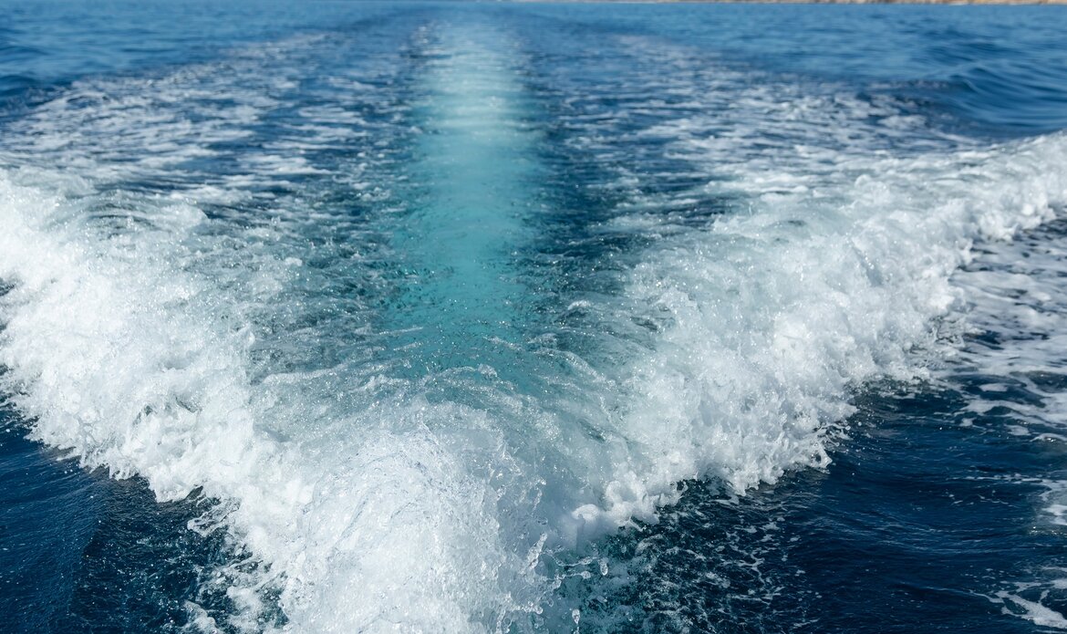 Ein Blick auf das klare, blaue Wasser mit Wellen, die hinter einem Boot entstehen. Die Spur im Wasser zeigt die Bewegung und Dynamik des Fahrens auf dem Meer.