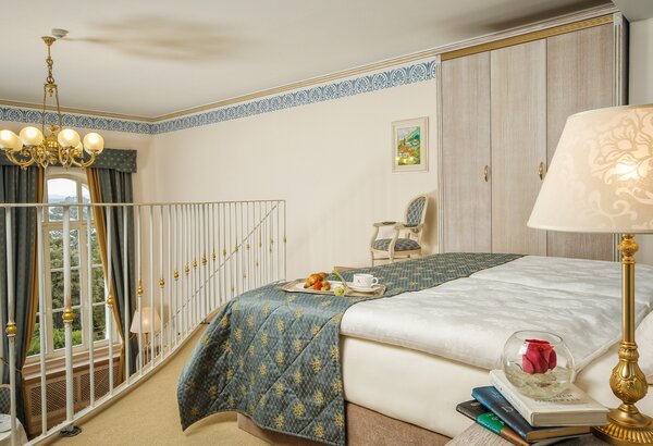 Ein elegantes Hotelzimmer mit einem großen Bett, einem Nachttisch und einer Lampe. Auf dem Bett liegen frisches Obst und eine Tasse. Im Hintergrund sind ein Stuhl und ein Kleiderschrank zu sehen. G... Kaiserliche Suiten im Hotel mit Meerblick Kroatien